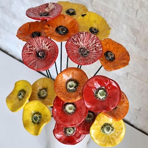 Peut inclure: Une collection de fleurs en céramique artisanale aux pétales rouge, orange et jaune vifs avec des finitions brillantes. Chaque fleur est fixée sur une fine tige en métal sombre, formant un bouquet de fleurs individuelles aux cœurs texturés.