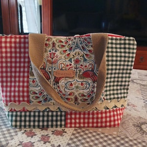 Puede incluir: Bolso tote hecho a mano con diseño patchwork. Presenta cuadros rojos y negros, un estampado floral y un asa beige. El panel central muestra un diseño floral y una etiqueta "Handmade". Con ribete festoneado.