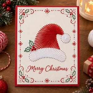Può includere: Un biglietto d'auguri rettangolare con bordo rosso caratterizzato da un design a filo teso raffigurante un cappello di Babbo Natale in filo rosso e bianco. Il biglietto include foglie di agrifoglio verdi con bacche rosse e la scritta Merry Christmas.
