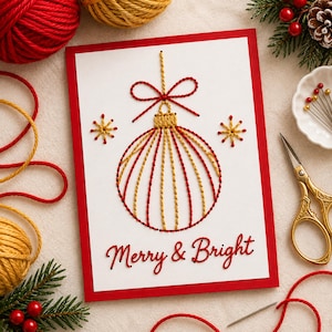May include: A white rectangular greeting card with a red border featuring an embroidered Christmas ornament design in red and gold thread. The ornament is topped with a red bow and flanked by two star shapes. The text Merry & Bright is stitched in red.