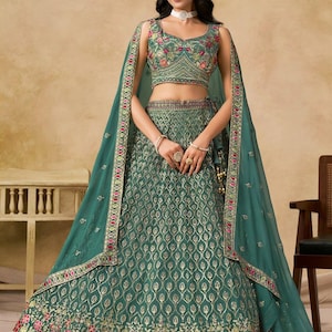 May include: A teal green formal dress with intricate gold embroidery and floral accents. The dress features a crop top, a long skirt, and a matching sheer shawl. The design includes a detailed pattern and is suitable for special occasions.