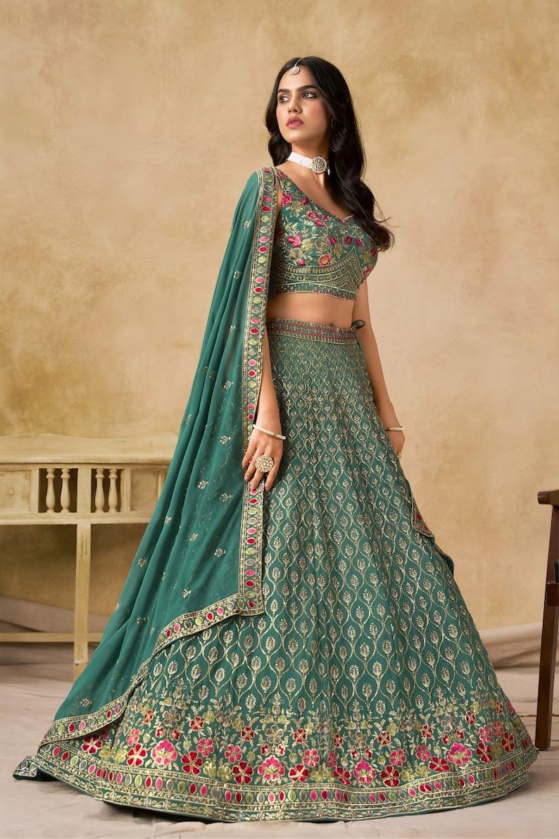 May include: Emerald green lehenga with intricate gold embroidery and floral accents. The ensemble includes a matching dupatta and a cropped top with floral embroidery. The skirt features a detailed pattern and a decorative border.