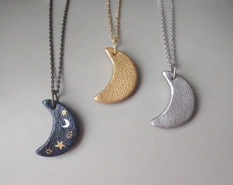 Puede incluir: Tres collares de media luna plateada, dorada y negra con cadenas delicadas. La luna negra tiene una media luna blanca y estrellas doradas pintadas.