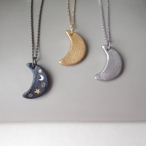 May include: Three silver, gold, and black crescent moon necklaces with delicate chains. The black moon has a white crescent moon and gold stars painted on it.