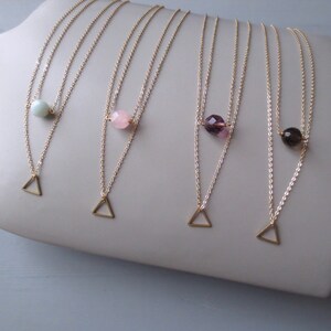Pode incluir: Quatro colares de ouro com um pingente triangular e uma única conta de pedra preciosa. Os colares apresentam uma variedade de pedras preciosas, incluindo verde, rosa, roxo e marrom.