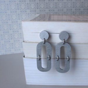 May include: A pair of silver earrings with a geometric design. The earrings are made of metal and have a brushed finish.