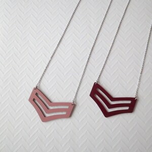 May include: Two silver chain necklaces with a chevron pendant. One pendant is pink and the other is burgundy.