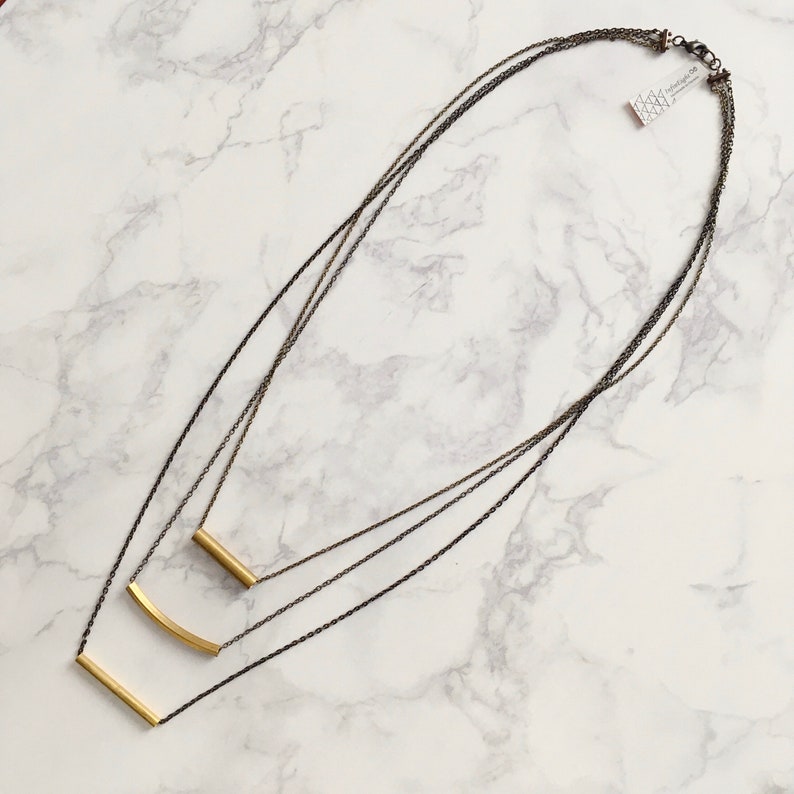 Puede incluir: Un collar de oro de varias capas con tres cadenas de diferentes longitudes y tres colgantes de barra de oro.