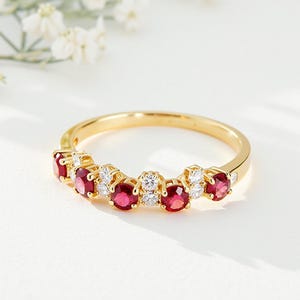 Puede incluir: Un anillo de oro con piedras preciosas rojas y claras alternadas. La banda del anillo es dorada y las piedras están dispuestas en una fila. Las piedras rojas son de un rojo intenso, las piedras claras son redondas.