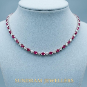 Puede incluir: Un collar con piedras preciosas rojas de corte ovalado alternando con piedras blancas redondas. El collar se exhibe sobre un maniquí azul. El texto "SUNDRAM JEWELLERS" está en la parte inferior de la imagen.