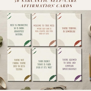 May include: A set of 56 sarcastic self-care affirmation cards. Each card features a unique quote in a serif font, with decorative color accents. The cards have a neutral background with phrases like "Rest is productive so is doing absolutely nothing."