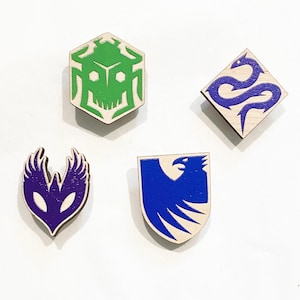 May include: Four wooden pins with colorful designs. One pin is a green hexagon with a skull-like design. Another is a blue diamond with a snake. A third is a purple, wing-like shape. The last is a blue shield with a bird.