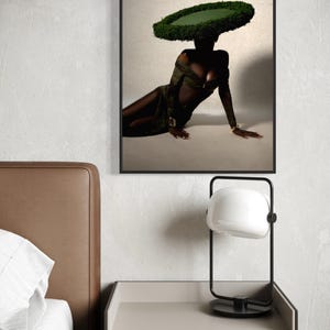 May include: A framed art print featuring a person wearing a large, circular green hat and a dark green dress. The person is seated on a light background. A black and white lamp sits on a nightstand.