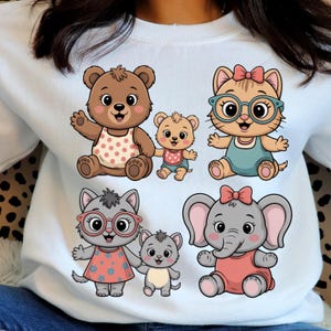 Peut inclure: Un sweat-shirt bleu clair orné d'illustrations de dessins animés d'un ours, d'un chat et d'un éléphant. L'ours porte un bavoir rose, le chat porte des lunettes et un nœud, et l'éléphant porte une robe rose. Le sweat-shirt est de style décontracté.