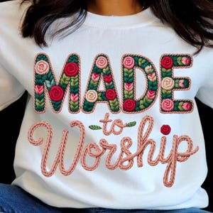 Peut inclure: Sweat-shirt blanc avec l'inscription brodée "MADE to Worship". Le mot "MADE" est en lettres florales vertes et roses. Les mots "to Worship" sont dans une police rose en forme de corde. Une rose rouge est au-dessus du mot "Worship".