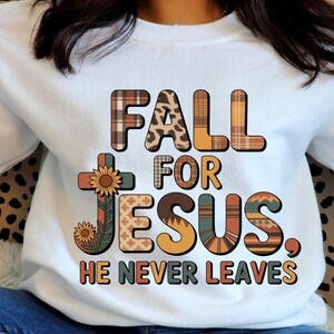 Peut inclure: Sweat-shirt blanc avec l'inscription "FALL FOR JESUS. HE NEVER LEAVES" dans différentes polices et couleurs à motifs. Une croix avec un tournesol est sur le côté gauche du motif. Vêtement religieux sur le thème de l'automne.