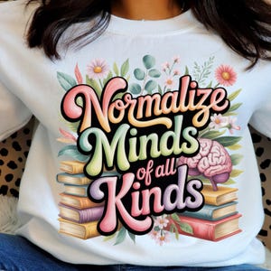 Peut inclure: Sweat-shirt blanc avec l'inscription "Normalize Minds of all Kinds" en lettres colorées et stylisées. Le motif comprend un cerveau, des livres et des éléments floraux. Vêtement décontracté et confortable.