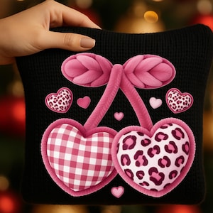 Peut inclure: Coussin noir avec un motif de cerise rose. Le motif de cerise présente deux cerises en forme de cœur, l'une avec un motif vichy rose et blanc et l'autre avec un imprimé léopard rose. Des cœurs roses supplémentaires et un nœud complètent le design.