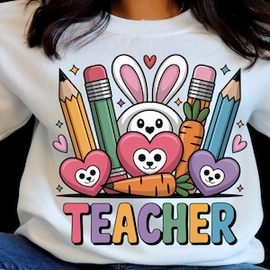 May include: White sweatshirt with a colorful graphic featuring a bunny, pencils, carrots, hearts, and the word "TEACHER". The design includes pink, orange, green, blue, and purple elements, perfect for educators.