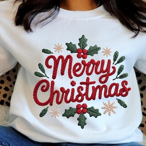 Peut inclure: Sweat-shirt blanc avec l'inscription brodée "Merry Christmas" en rouge, entourée de feuilles de houx vertes, de baies rouges et de flocons de neige beiges. Vêtement de fête sur le thème des fêtes.