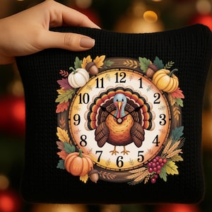 May include: A black pillow featuring a Thanksgiving-themed clock design. The clock face has a turkey in the center, surrounded by pumpkins, leaves, and wheat. The clock hands point to 1:50. The pillow is held by a hand.