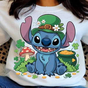 Peut inclure: Sweat-shirt blanc avec un personnage de dessin animé bleu portant un chapeau vert orné de fleurs blanches. Le motif comprend des trèfles verts, un champignon rouge et blanc et un pot de pièces d'or. Thème de la Saint-Patrick.