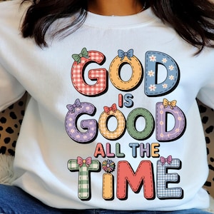 Peut inclure: Un sweat-shirt blanc avec l'inscription "GOD IS GOOD ALL THE TIME" en lettres colorées de style patchwork. Les lettres sont ornées de nœuds et de motifs floraux, créant un design joyeux et motivant.