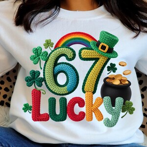 Peut inclure: Sweat-shirt blanc avec un motif coloré de la Saint-Patrick. Comprend un arc-en-ciel, un chapeau de lutin vert, un pot d'or et les chiffres "67" avec le mot "LUCKY". Comprend des trèfles dans le design.