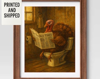May include: A framed wall art print featuring an oil painting of a brown turkey sitting on a white toilet in a wooden bathroom, reading a newspaper titled The Turkey Times. The scene includes a toilet paper roll holder and a towel on the wall.