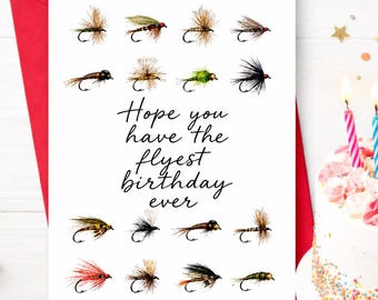 May include: A white greeting card featuring a grid of various colourful fishing fly illustrations and the black cursive text Hope you have the flyest birthday ever. The card is positioned on a red envelope against a white surface.