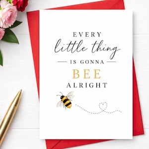 May include: A white greeting card with black and gold text that reads EVERY little thing IS GONNA BEE ALRIGHT. The card features a small illustration of a yellow and black bumblebee with a dotted line path ending in a heart shape.