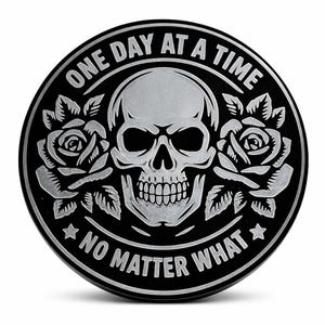 May include: A black and silver round emblem featuring a skull, roses, and the phrases "ONE DAY AT A TIME" and "NO MATTER WHAT". The skull is in the center, with roses on either side.