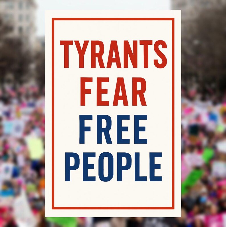 May include: A rectangular sign with a red border and the words "TYRANTS FEAR FREE PEOPLE" in bold red and blue text. The background is a blurred image of a crowd of people.