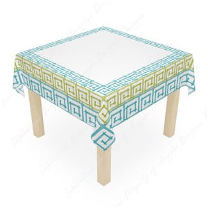May include: A square tablecloth featuring a white centre and a decorative border with a repeating geometric Greek key pattern in alternating shades of lime green and turquoise blue, draped over a four-legged wooden table with a light finish.