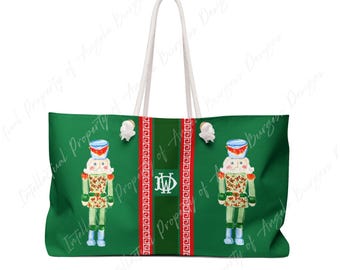May include: A green tote bag featuring two nutcracker illustrations, one on each side of a central dark green vertical stripe. The stripe is flanked by two red bands with a white Greek key pattern. A white monogram with the letters JW is centered.