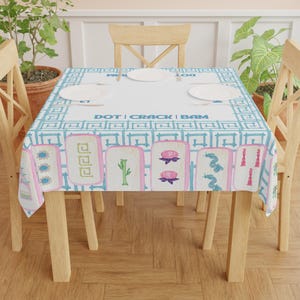 May include: A rectangular tablecloth featuring a light blue and white geometric pattern with the words "DOT | CRACK | BAM". The tablecloth has illustrations of Mahjong tiles in pink, green, and blue.