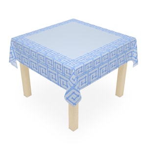 May include: A square tablecloth with a light blue center and a patterned border in a darker shade of blue. The tablecloth is draped over a square table with four light-colored wooden legs.