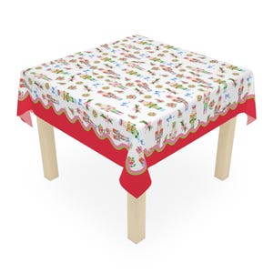 May include: A square tablecloth featuring a white top surface with a repeating pattern of nutcracker figures, floral motifs, and blue bows. The edges are finished with a scalloped green trim and a solid red border, draped over a light wood table.