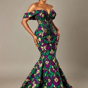 Op de afbeelding: Een off-the-shoulder, vloerlange jurk met een getailleerd lijfje en een uitlopende rok. De jurk heeft een levendig geometrisch patroon in groen, paars en goud. Het lijfje heeft een korsetachtig ontwerp en de stof heeft een lichte glans.