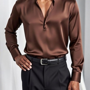 Può includere: Una camicia di raso marrone con scollo a V e maniche lunghe. La camicia è abbinata a pantaloni neri e una cintura in pelle nera con fibbia argentata. L'outfit è uno stile formale.