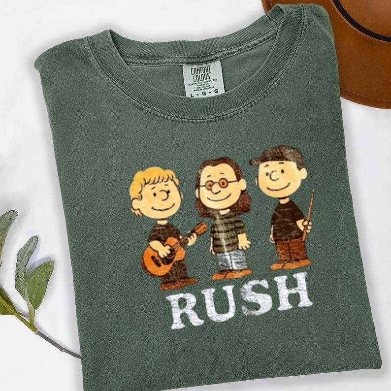 Peut inclure: T-shirt vert fonc&eacute; avec une illustration de dessin anim&eacute; de trois personnages, chacun avec un instrument de musique ou une baguette de chef d'orchestre. Le mot "RUSH" est imprim&eacute; en lettres blanches en dessous.