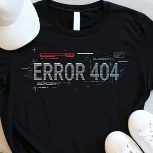 May include: Black t-shirt with the text "ERROR 404" in white, featuring a digital glitch design with red and blue accents. A white baseball cap and white sneakers are visible in the image.