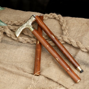 K&ouml;nnte beinhalten: Ein h&ouml;lzerner Spazierstock mit einem dekorativen Messinggriff und Akzenten. Der Griff weist ein verziertes Blumendesign auf. Der Stock ist braun mit Messingdetails und einer schwarzen Gummispitze. Der Stock ist etwa 91 cm lang.