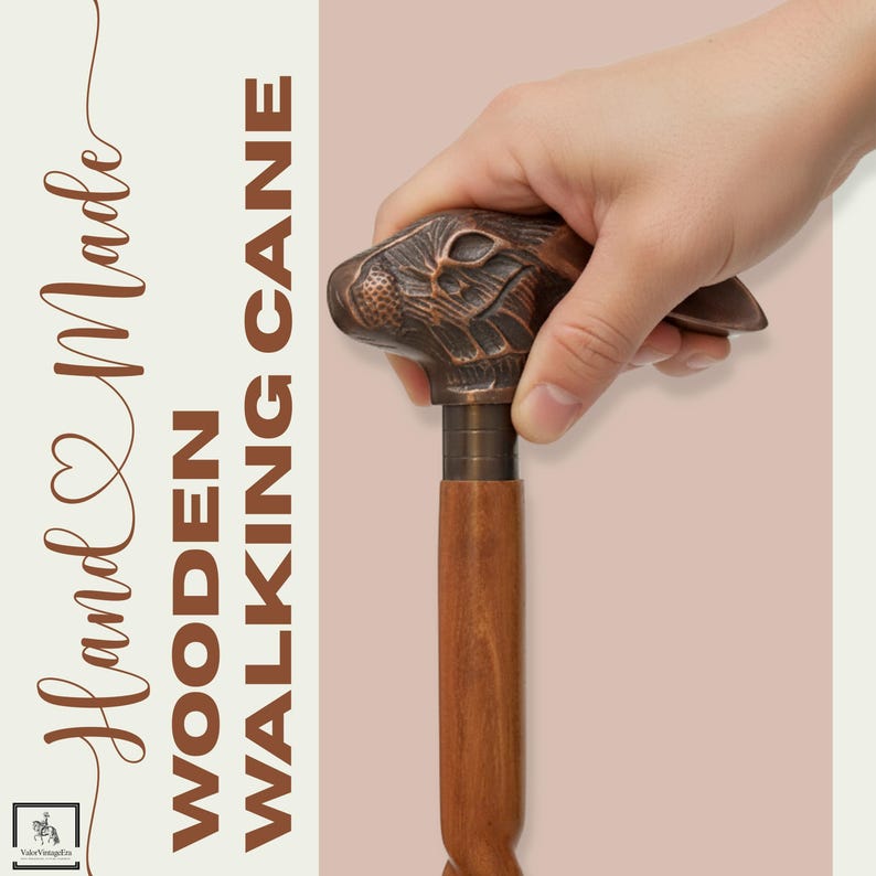 May include: Hand-carved wooden walking cane with a bronze-colored rabbit head handle. The cane has a dark brown wooden shaft and a bronze-colored metal collar. The text "Hand Made WOODEN WALKING CANE" is printed on the left side.