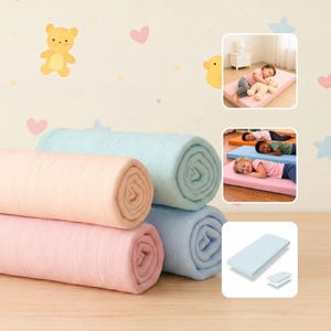 May include: Rolled pastel-colored blankets in pink, blue, and green are stacked on a wooden surface. The image also shows children sleeping on rectangular mats in various colors. The background features cartoon bears and hearts.