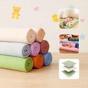 May include: A stack of rolled-up, colorful blankets in shades of pink, beige, blue, green, purple, orange, and brown. The image also shows children sleeping on colorful mats and a diagram of the mat's layers. Decorative wall stickers include a yellow bear and duck.