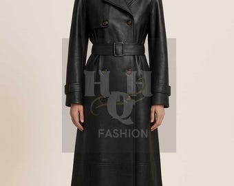 Op de afbeelding: Een lange, zwarte, dubbelrijige trenchcoat met een brede kraag, lange mouwen met manchetten en een bijpassende riem met een rechthoekige gesp. De jas heeft een gladde afwerking en reikt tot aan de enkels. De tekst HQ FASHION is zichtbaar.