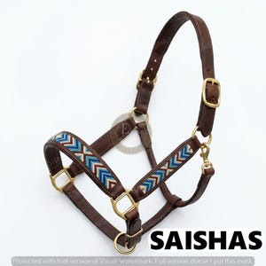 May include: A brown leather horse halter featuring brass hardware and decorative beadwork in a chevron pattern of blue, white, and maroon. The halter includes adjustable straps with metal buckles and a snap hook, with the text SAISHAS visible.