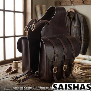 Könnte beinhalten: Dunkelbraune Ledersatteltaschen mit Messing-Schnallen und Riemen. Die Taschen haben eine Vintage-Ästhetik und werden auf einer Holzoberfläche präsentiert. Die Taschen sind für den Reitsport konzipiert.