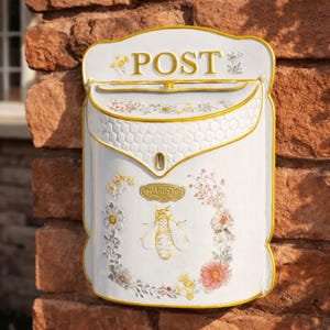 May include: White metal mailbox with gold trim and floral and bee accents. The word "POST" is displayed in gold lettering at the top. A decorative bee and the word "GARDEN" are featured on the front.